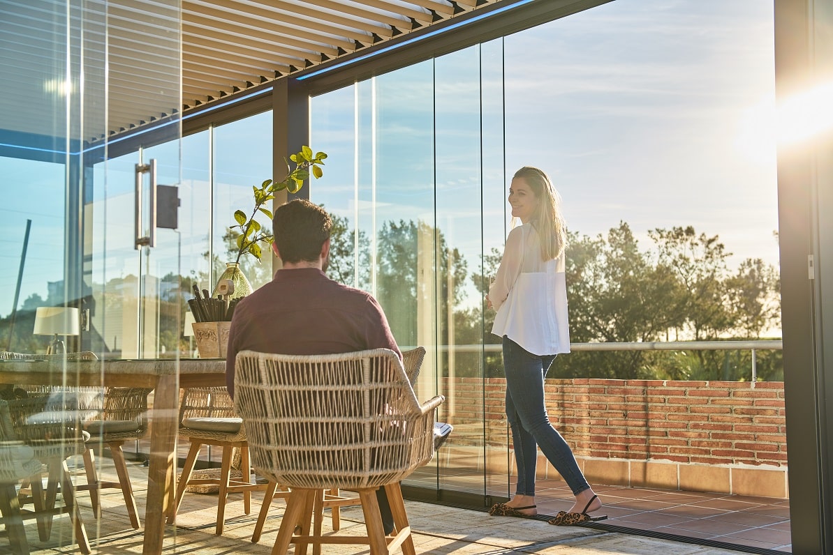 Mujer abriendo cortina de cristal corredera en su terraza delante de su marido