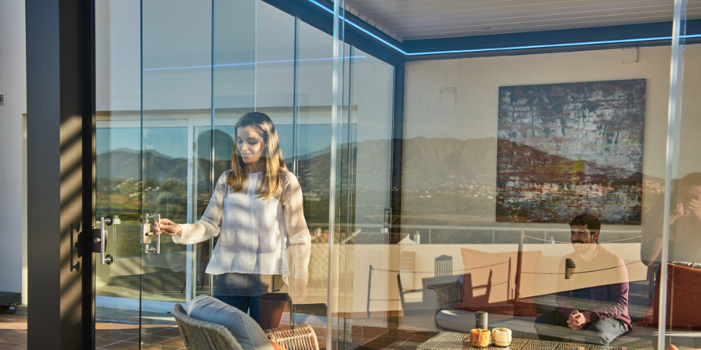 una pareja abre cortinas de cristal en una terraza
